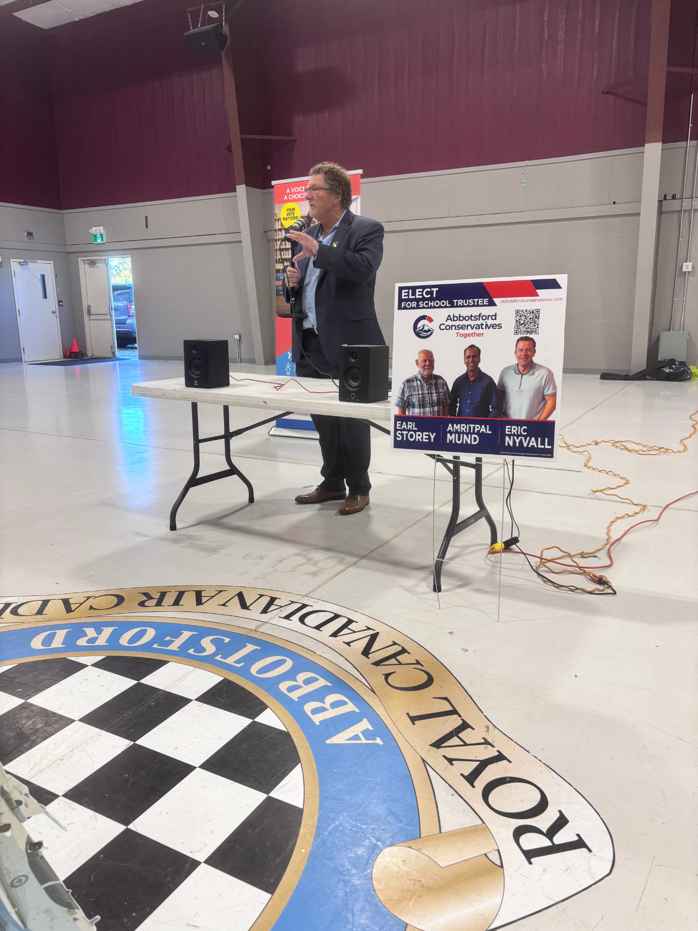 Earl Storey speaking at the School Trustee Candidate Meet & Greet at the Abbotsford Cadet Hall, beside his campaign sign